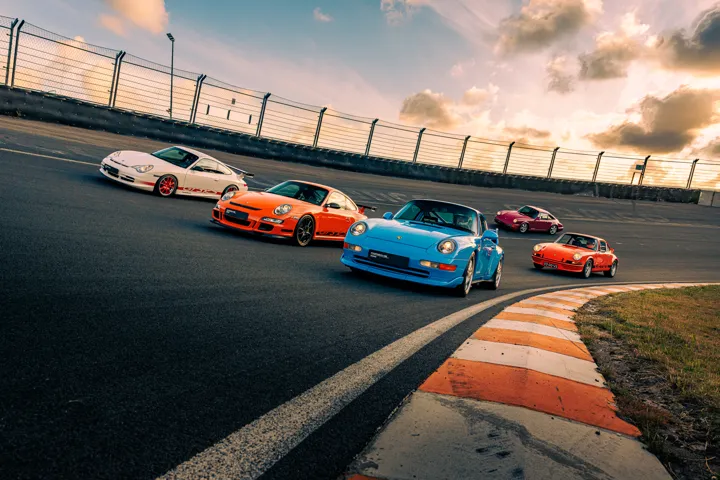 Porsche sports cars driving around a banked circuit in warm evening light.