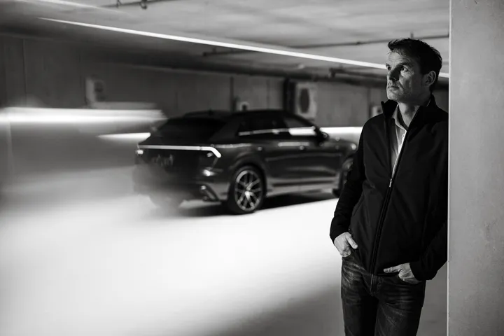 Black-and-white portrait beside an Audi Q8 in a parking garage.