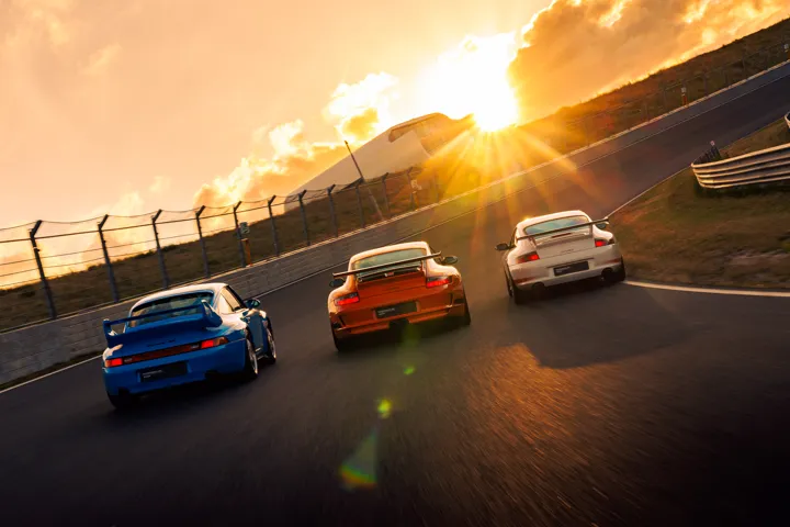 Porsche sports cars on a banked circuit at sunset.