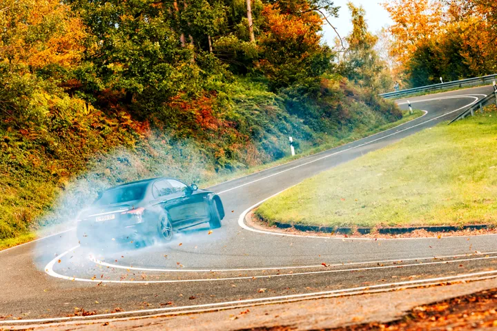 A performance car rounding a winding road through autumn trees.