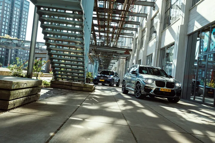 BMW and Mercedes-AMG performance SUVs beneath a steel bridge.