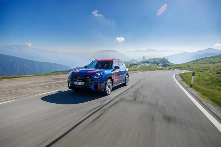 A blue and red MINI driving along a sunlit mountain road.